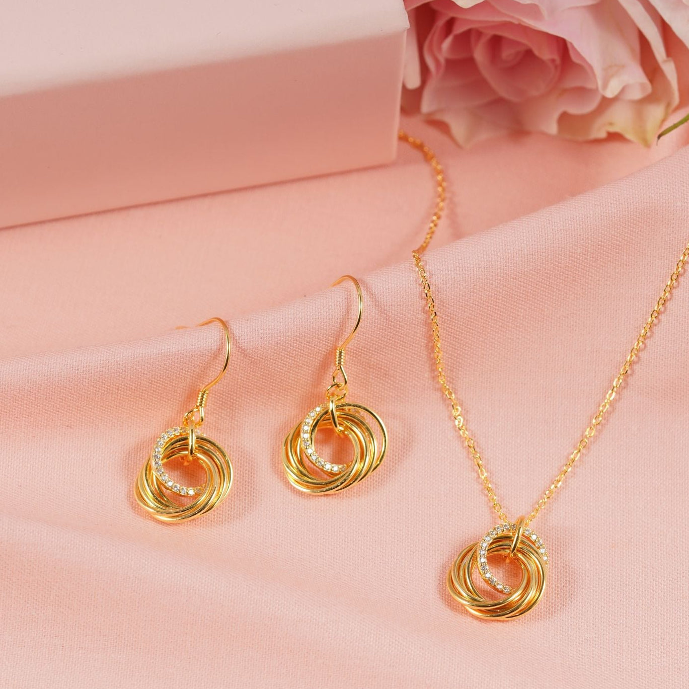 Gold jewelry set with earrings and necklace on a pink fabric background, featuring 'ANNABEL JEWELLERY'.