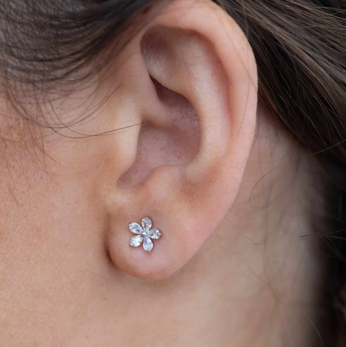 Close-up of an ear wearing a floral earring with clear stones.