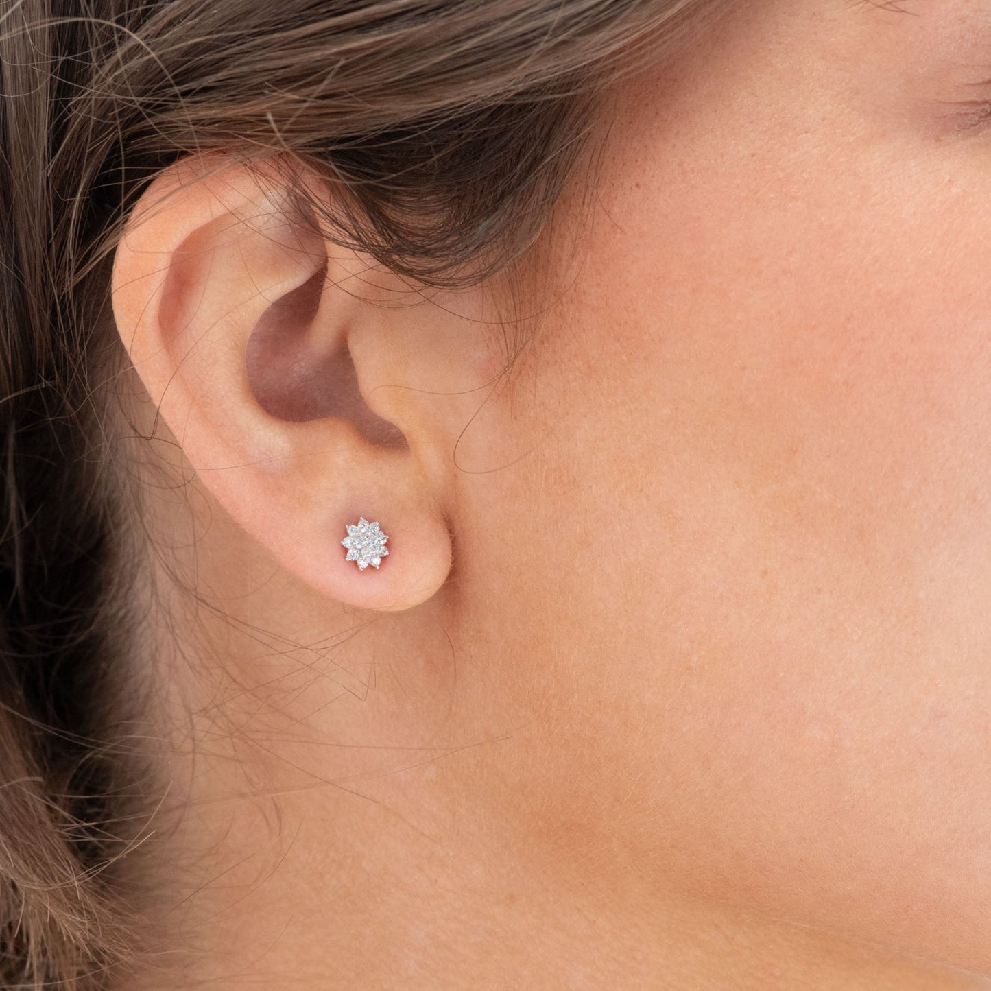Close-up of a woman wearing diamond stud earrings with a light blue background