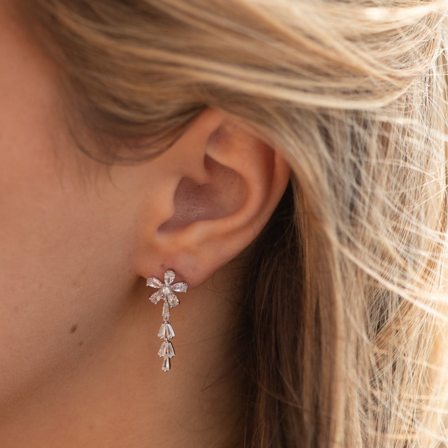 Close-up of a woman's ear wearing a diamond earring with blonde hair.