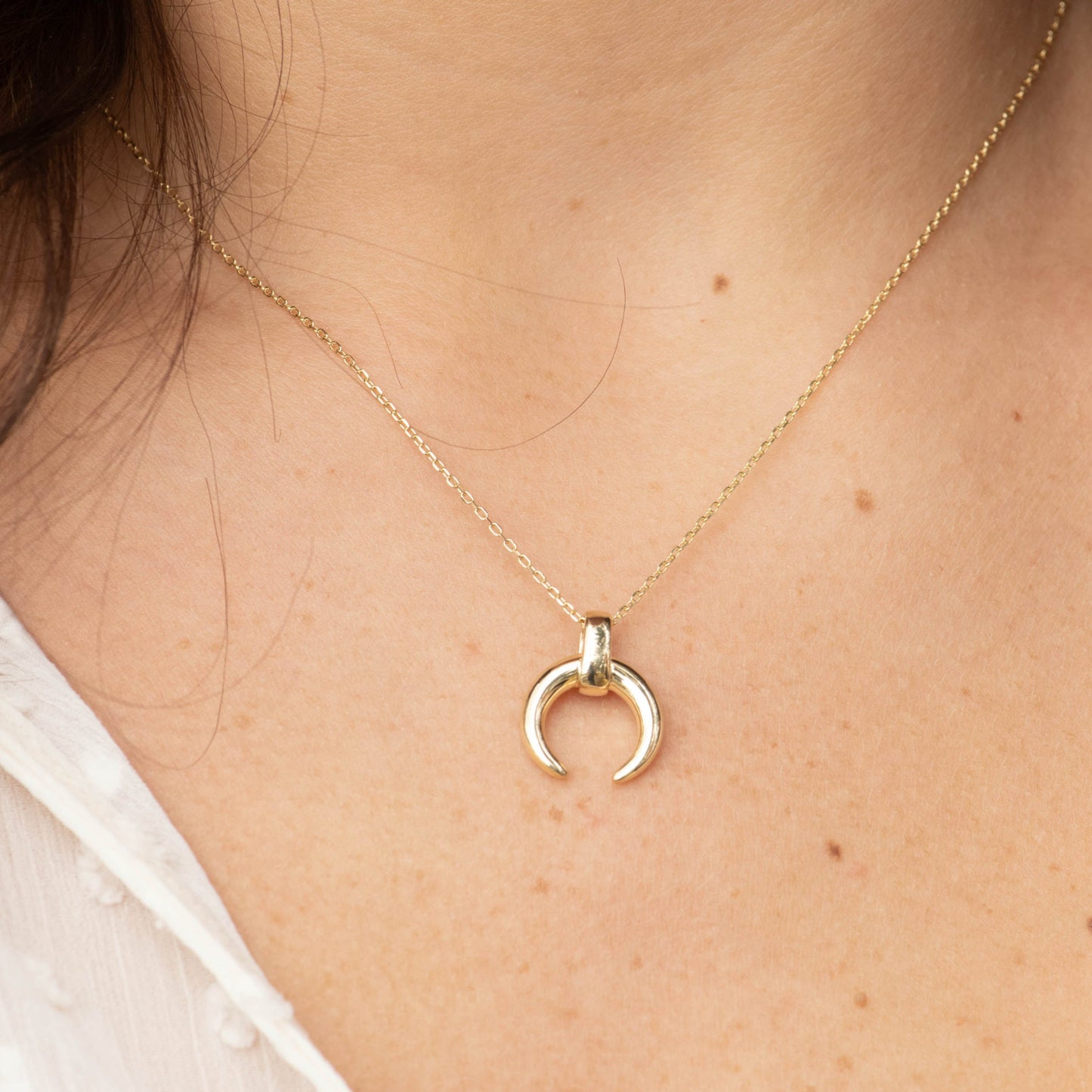 Gold necklace with a small pendant on a person wearing a white blouse.