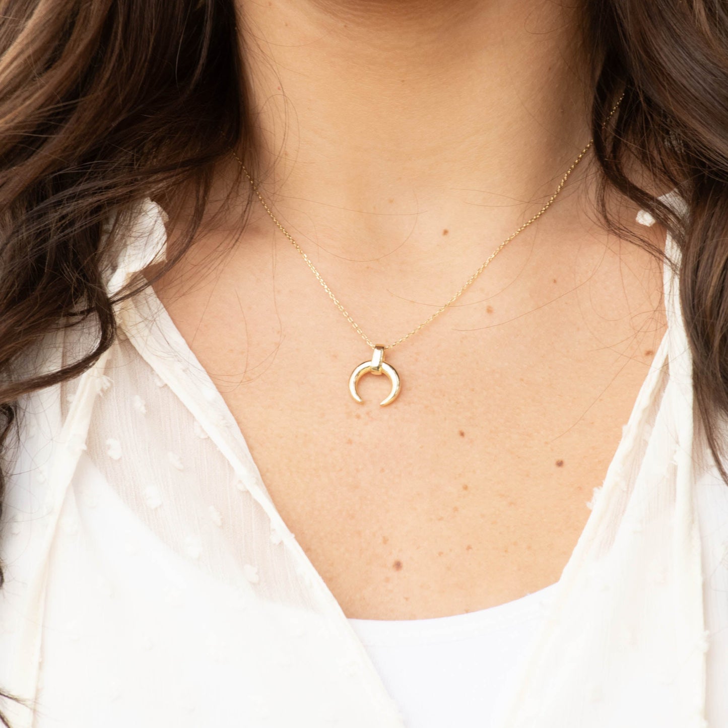 Close-up of a person wearing a delicate gold moon necklace.