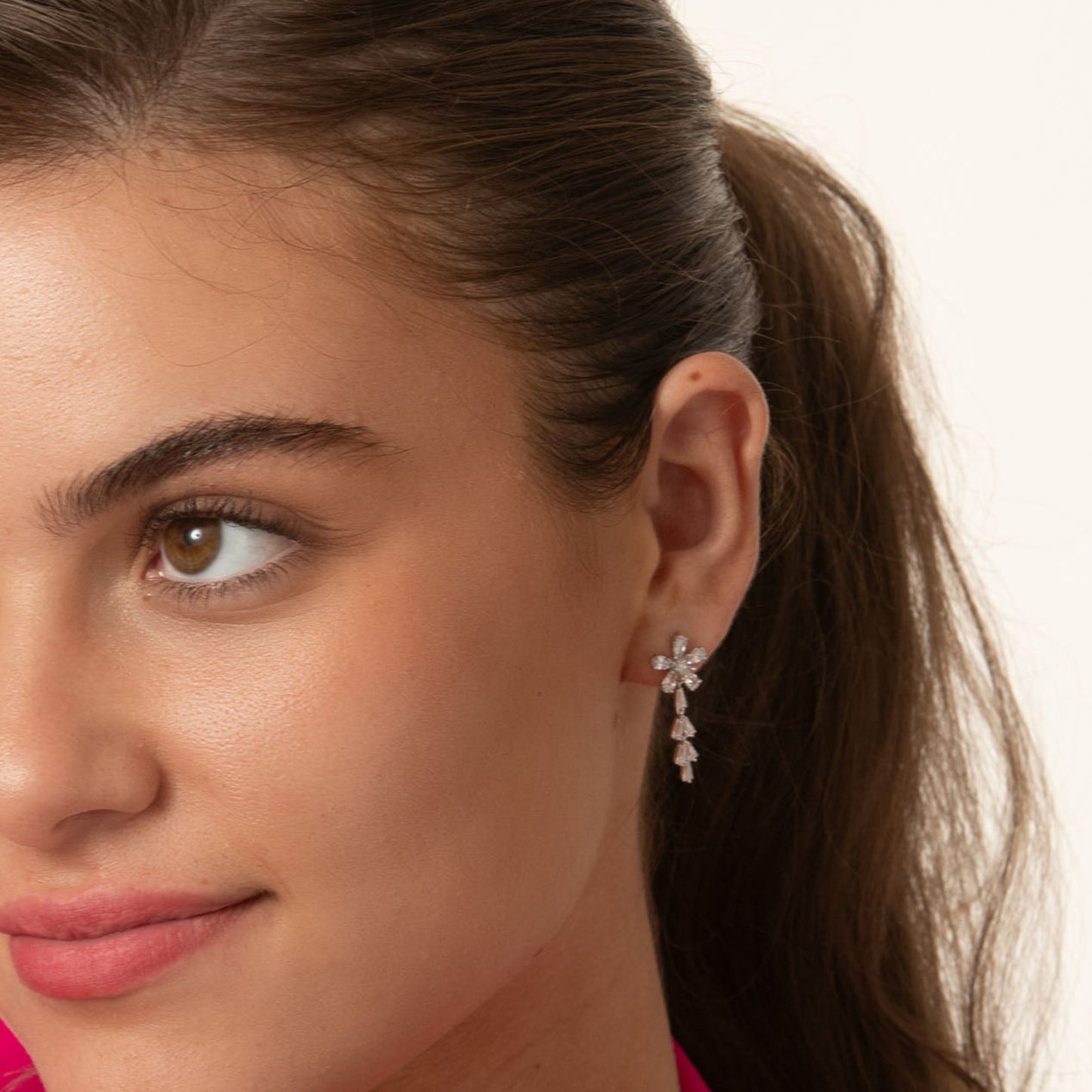 Woman wearing a bright pink blazer against a plain background with dainty drop earrings