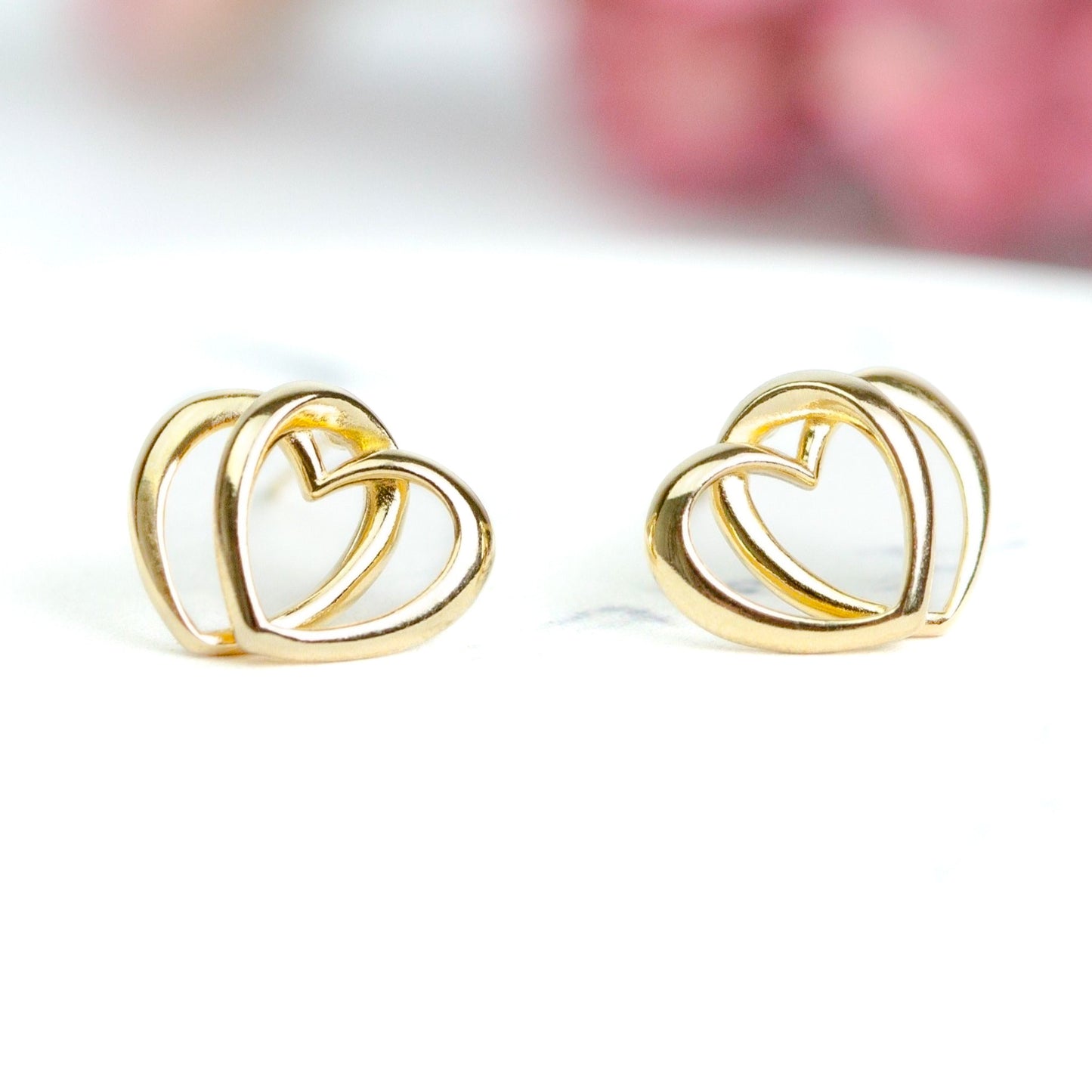 A pair of gold-colored heart-shaped stud earrings on a white background.