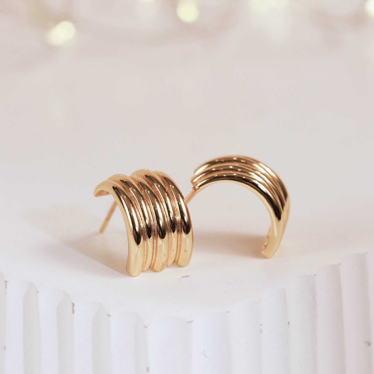 Gold hoop earrings on a white surface with a soft focus background