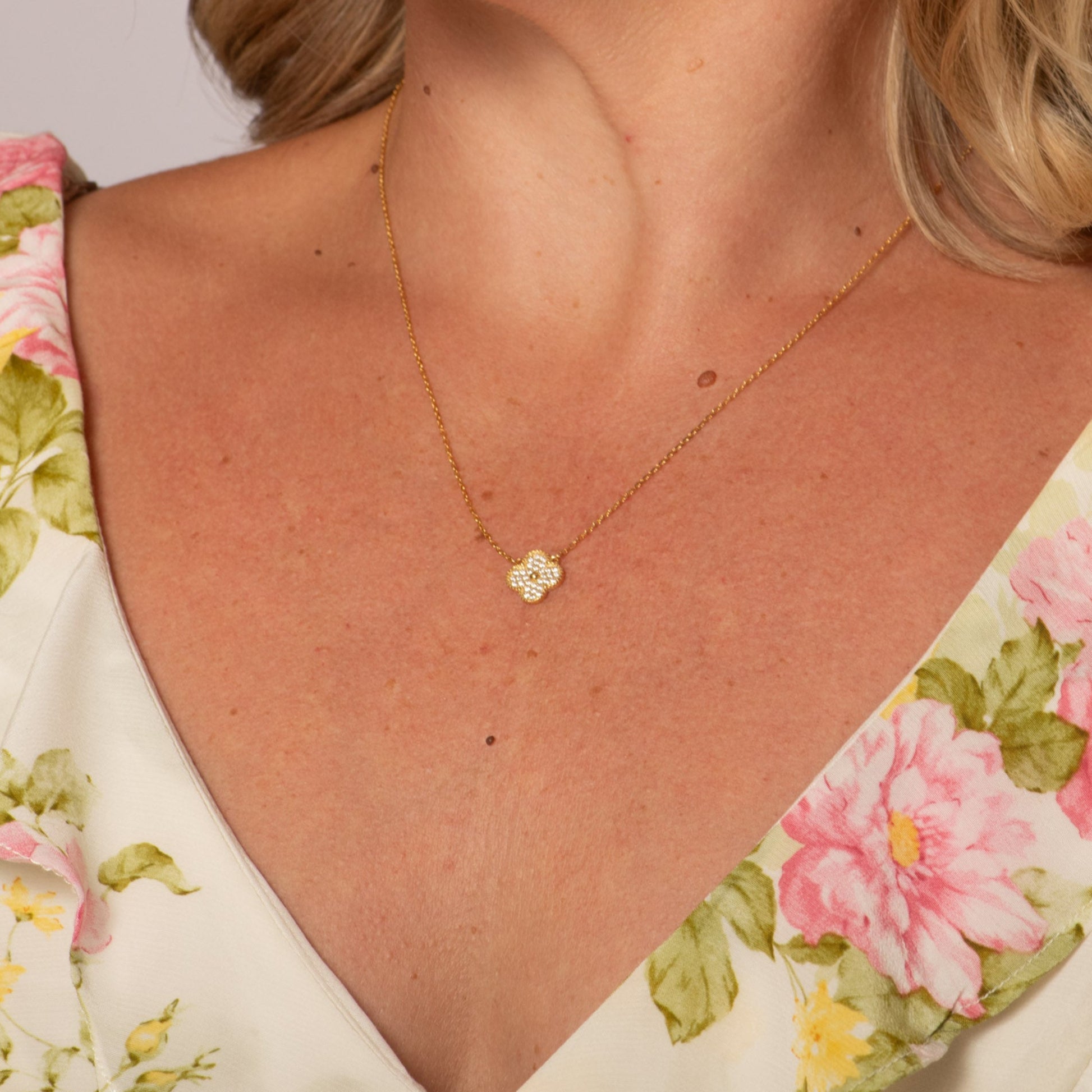 chest of woman in floral dress wearing gold plated clover necklace