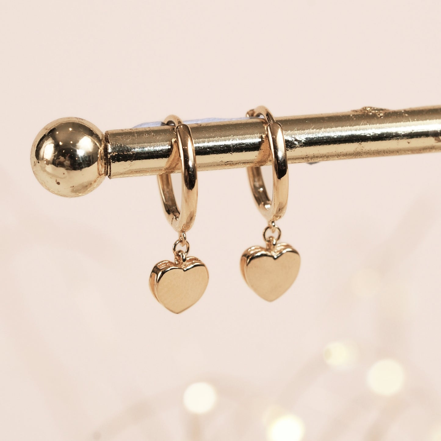 Gold hoop earrings with heart-shaped charms on a light pink background