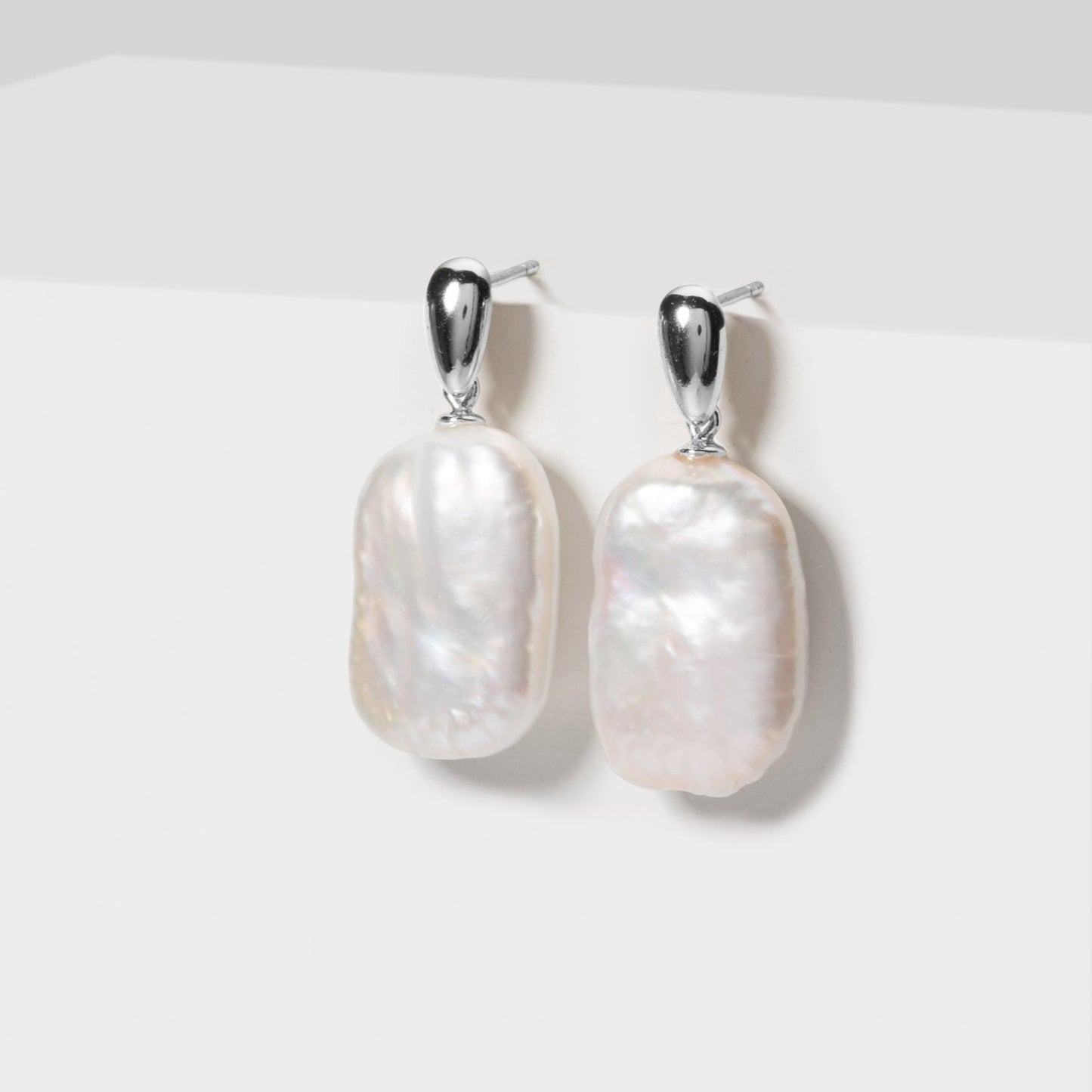 Pair of pearl earrings on a white pedestal against a light gray background
