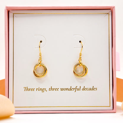 Gold circular drop earrings with braided texture, dangling from hook ear wires