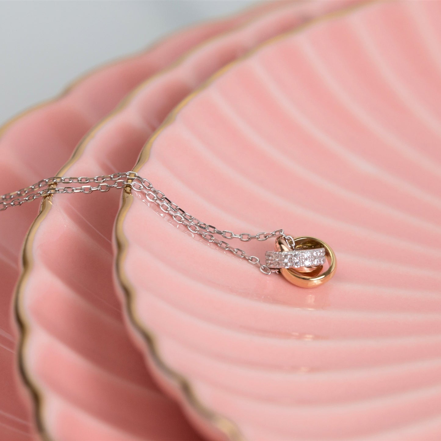 Necklace with a gold and silver pendant on a pink dish