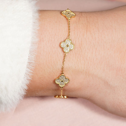 Gold clover bracelet with three shimmering clover charms on a fine chain, on wrist.