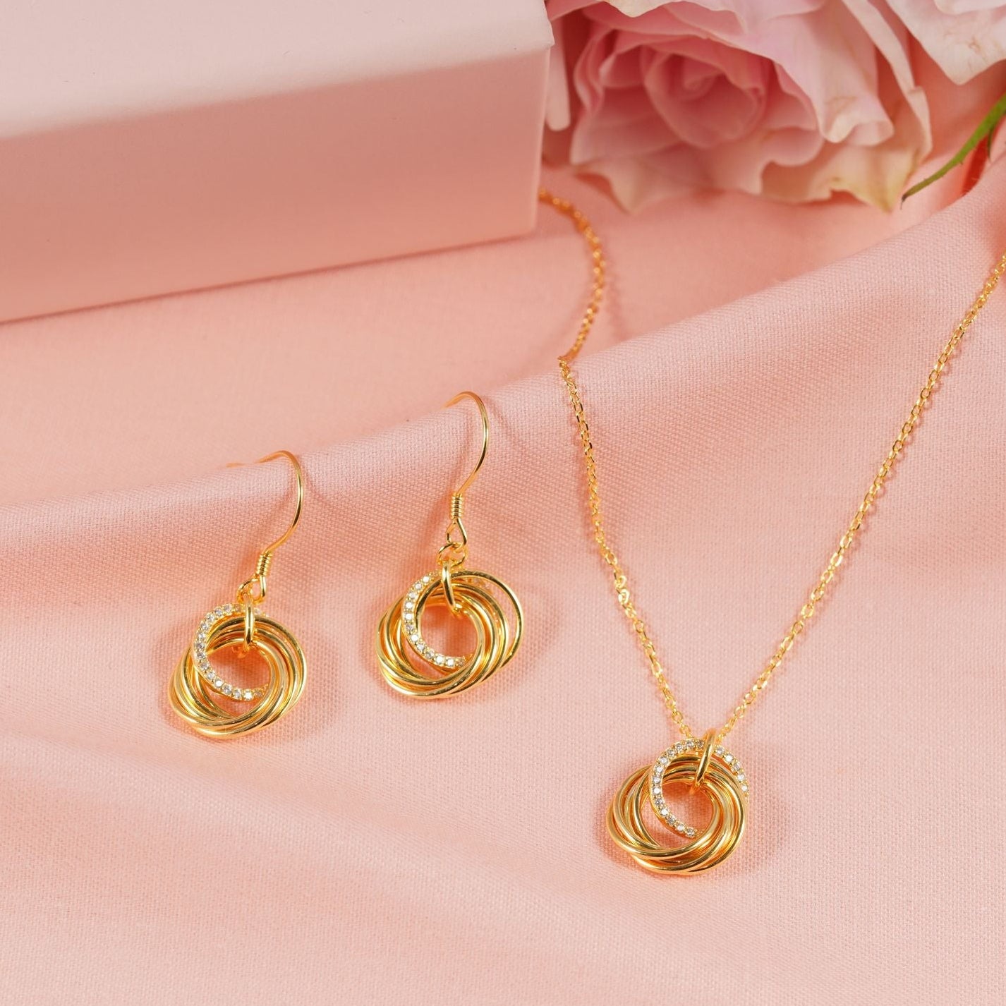 Gold jewelry set with earrings and necklace on a pink fabric background, featuring 'ANNABEL JEWELLERY'.