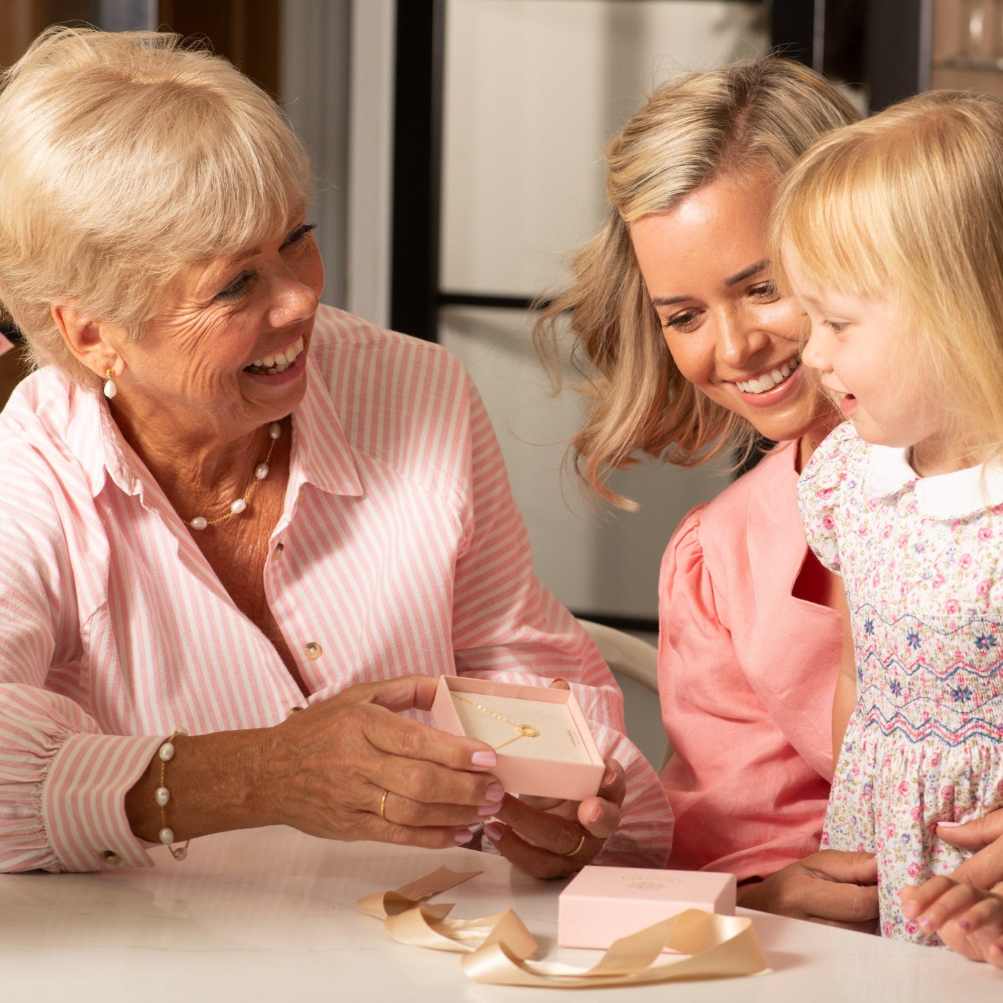 Three generations of women looking at a small jewellery gift box together in a kitchen.