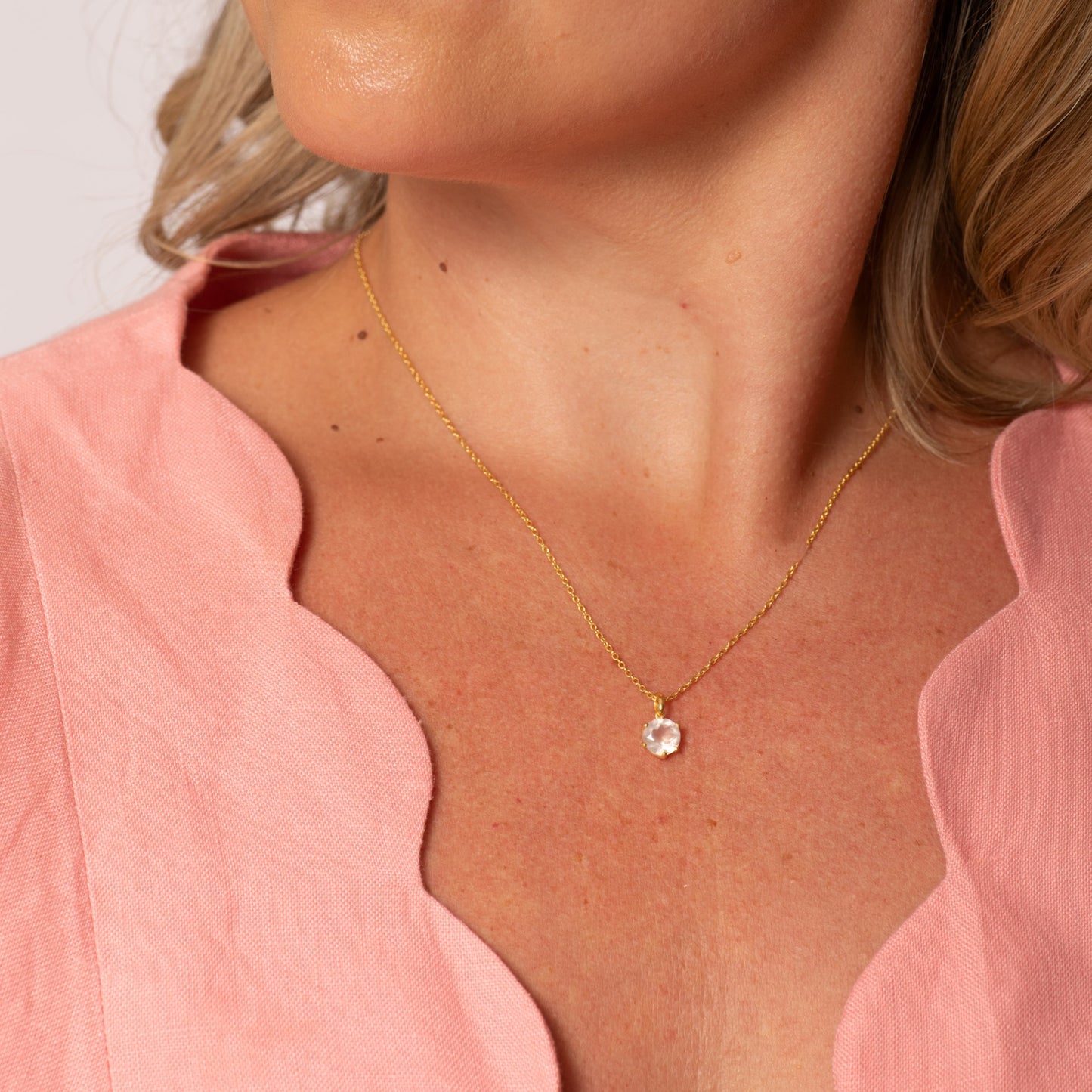 Gold pendant necklace worn with small purple gemstone charm