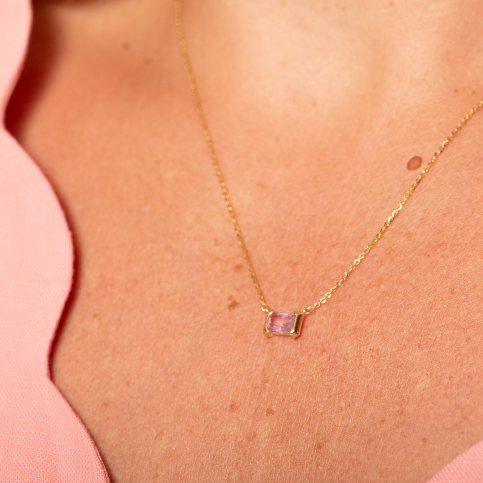 Gold necklace with a pink gemstone pendant on a person wearing a pink top.
