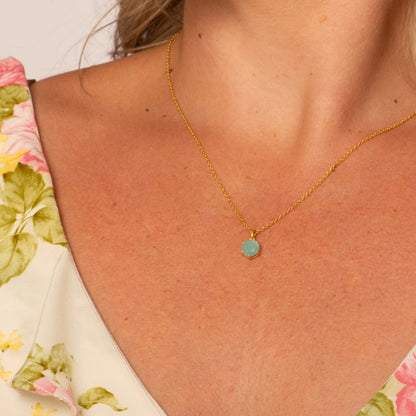 Gold chain necklace with round blue-green pendant at center