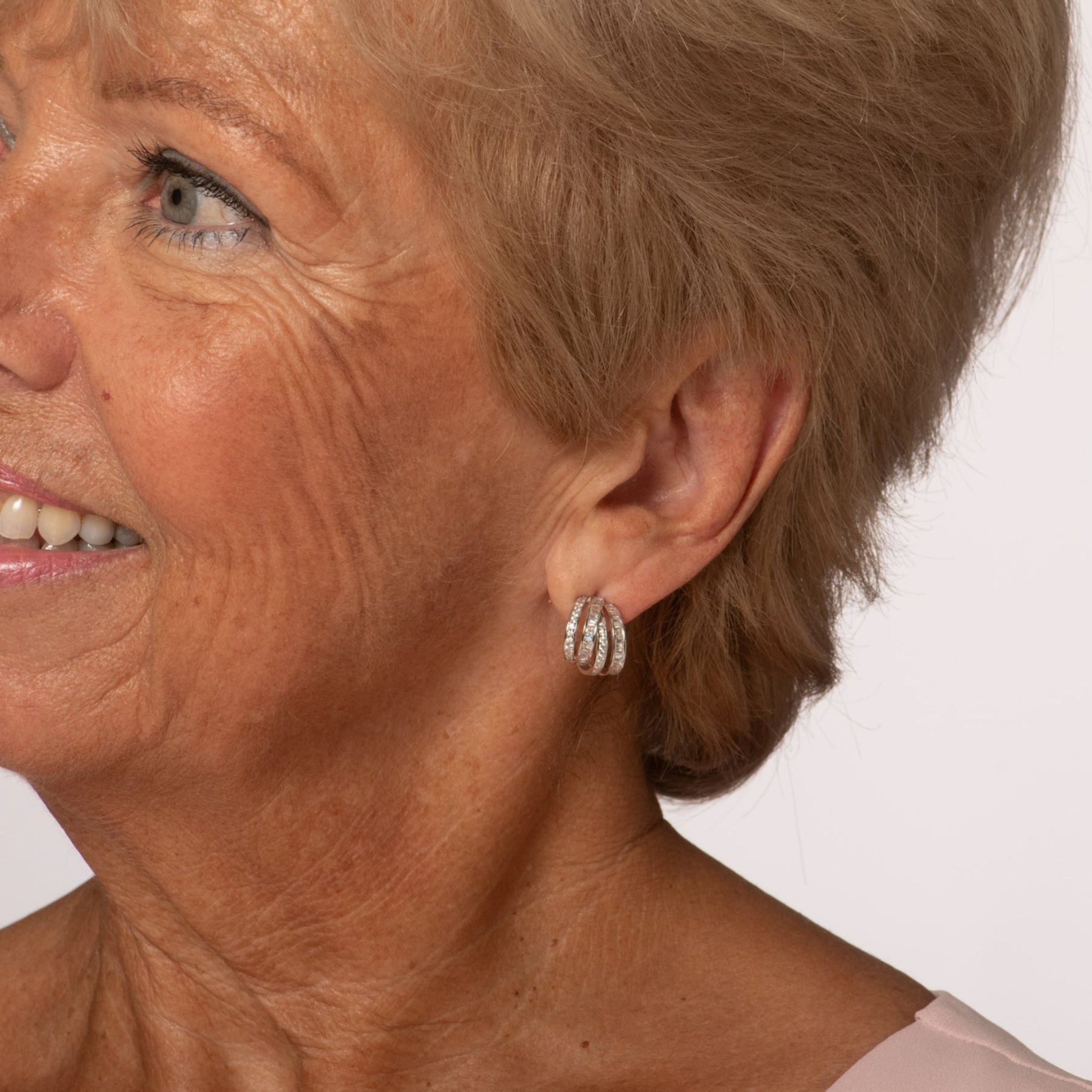 Woman with short blonde hair wearing earrings against a plain background