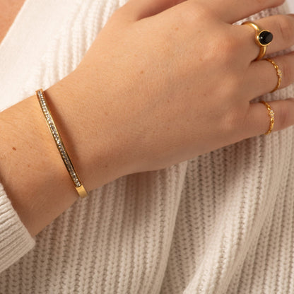 Gold crystal bangle on wrist, slender hinged cuff with clear stone row