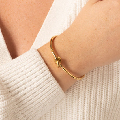 Gold knot bangle bracelet on wrist with twisted ring clasp detail