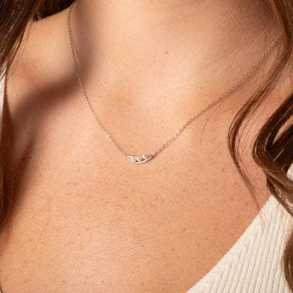 Silver peas-in-a-pod necklace worn on neckline, three faux pearl pods on chain