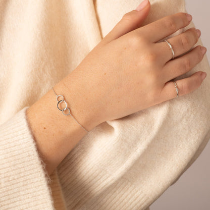 Silver chain bracelet with three linked ring charms on wrist