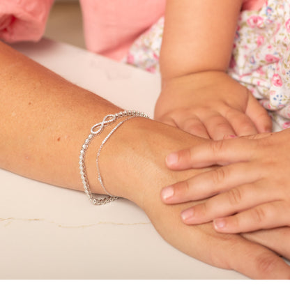 Silver infinity charm bracelet on wrist with linked pavé band