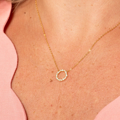 Gold circle pendant necklace with small stone halo on a fine chain