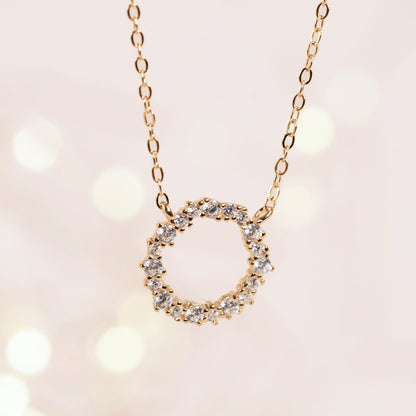 Gold circle pendant necklace with round halo of small stones on a chain