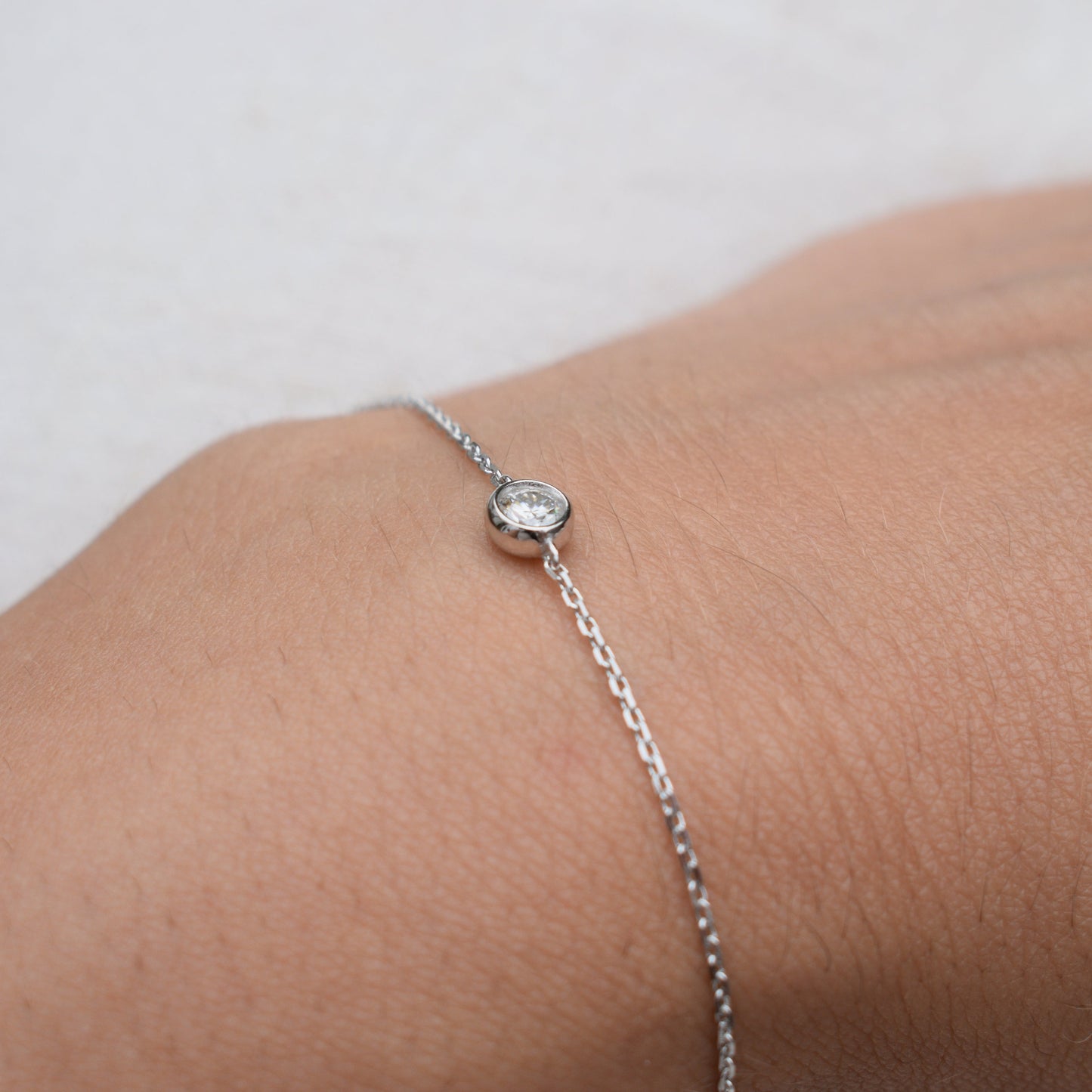 Close-up moissanite bracelet with round bezel-set stone on silver chain
