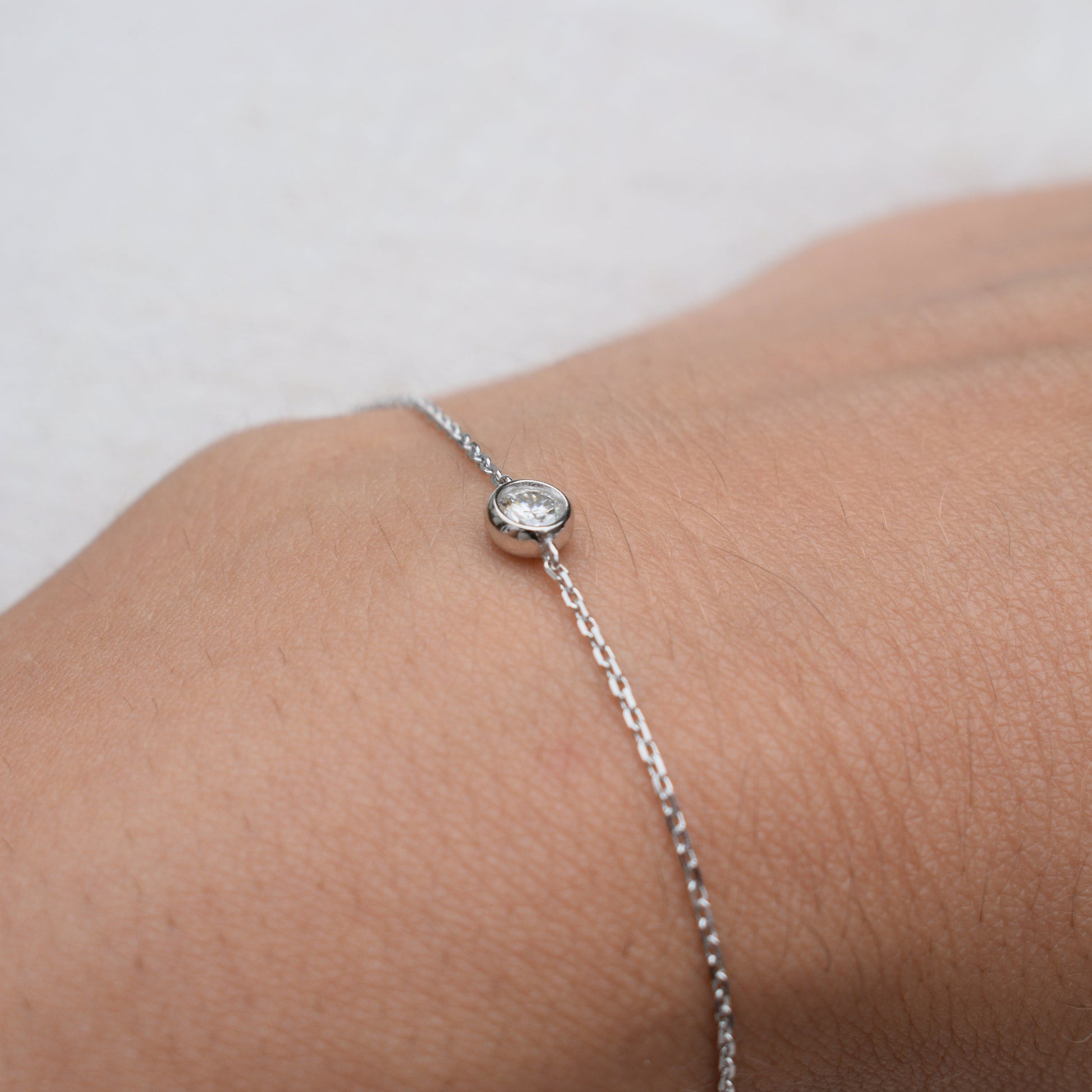 Close-up moissanite bracelet with round bezel-set stone on silver chain