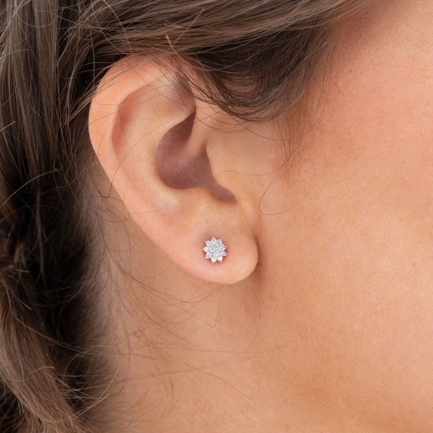 Sterling silver dainty flower stud earrings on ear, round pave design