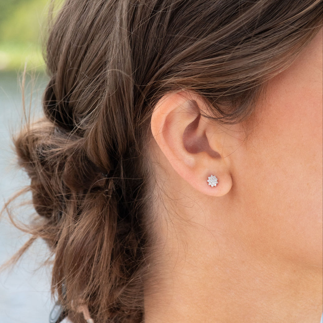 Sterling silver floral stud earrings with small sparkle, shown from side on ear