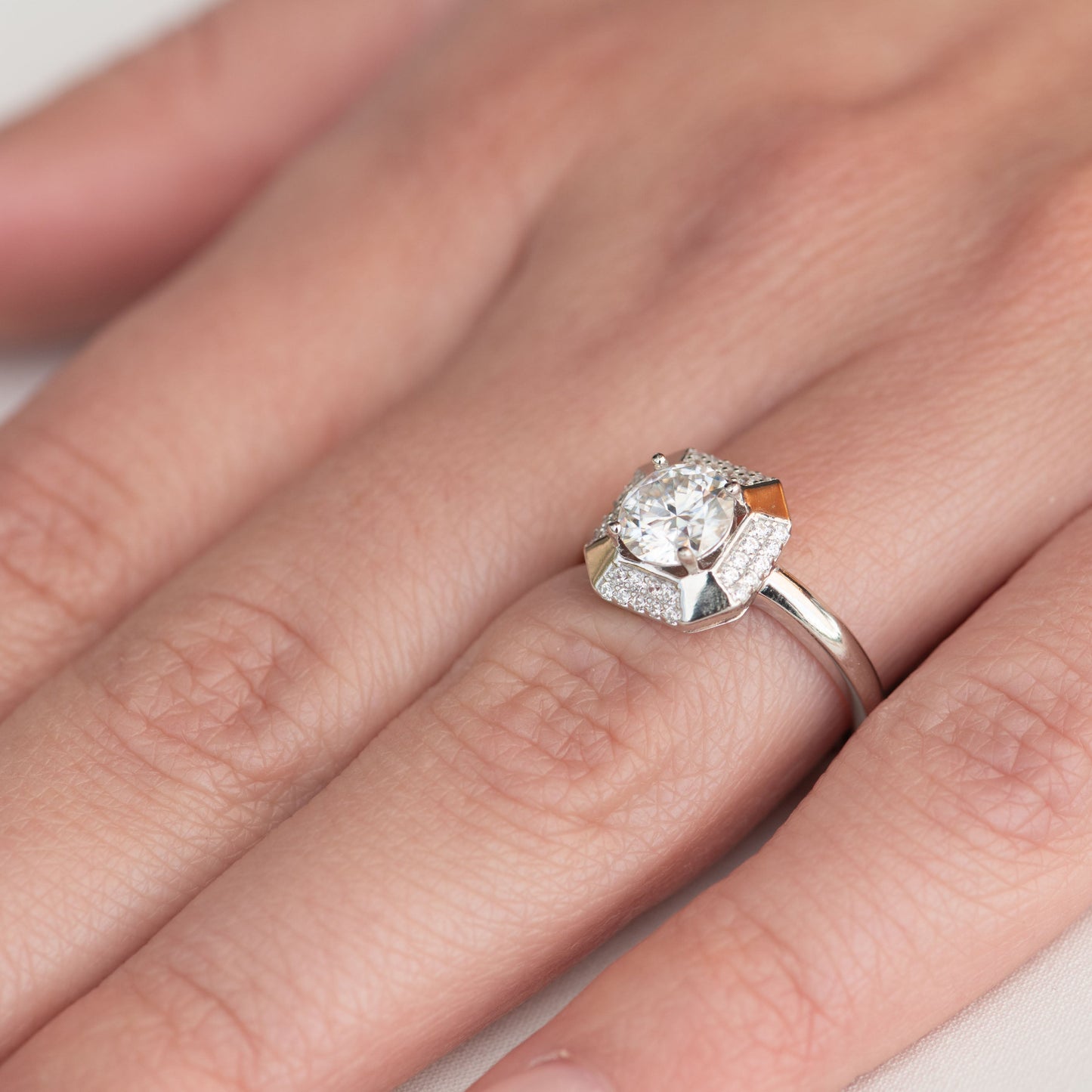 Silver ring with a diamond on a hand against a neutral background