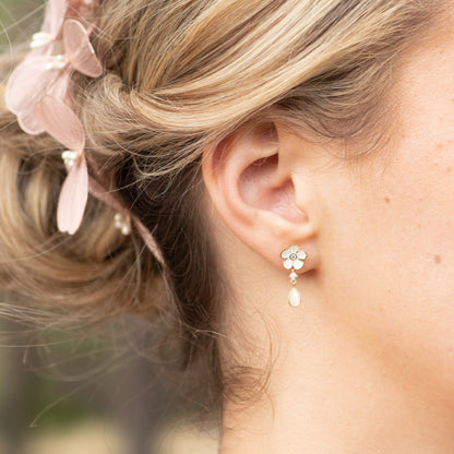 Gold-tone flower stud earrings with white enamel petals and dangling teardrop drop