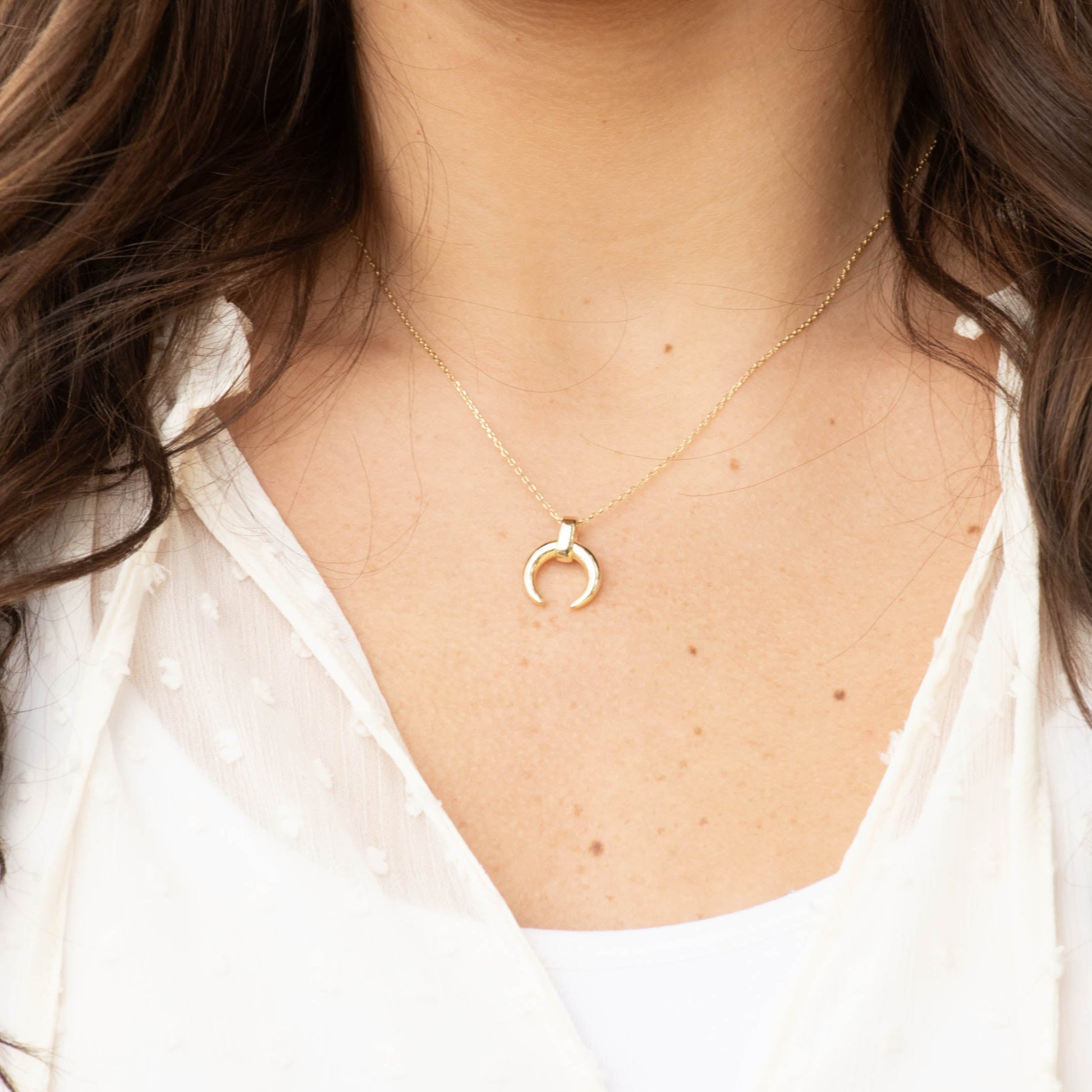 Close-up of a person wearing a delicate gold moon necklace.