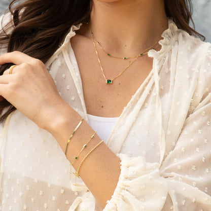 Gold-tone CZ baguette necklace with emerald green rectangular stones, layered on neck