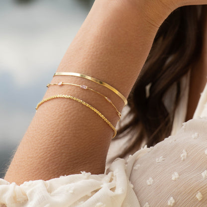 Snake chain necklace in gold tone, layered on wrist with curved link texture