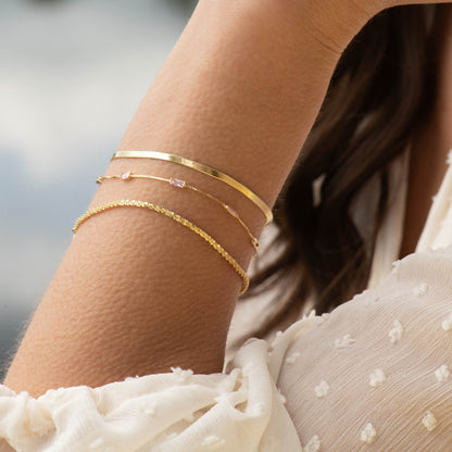 Gold flat snake chain bracelet set on wrist with slim bar clasp