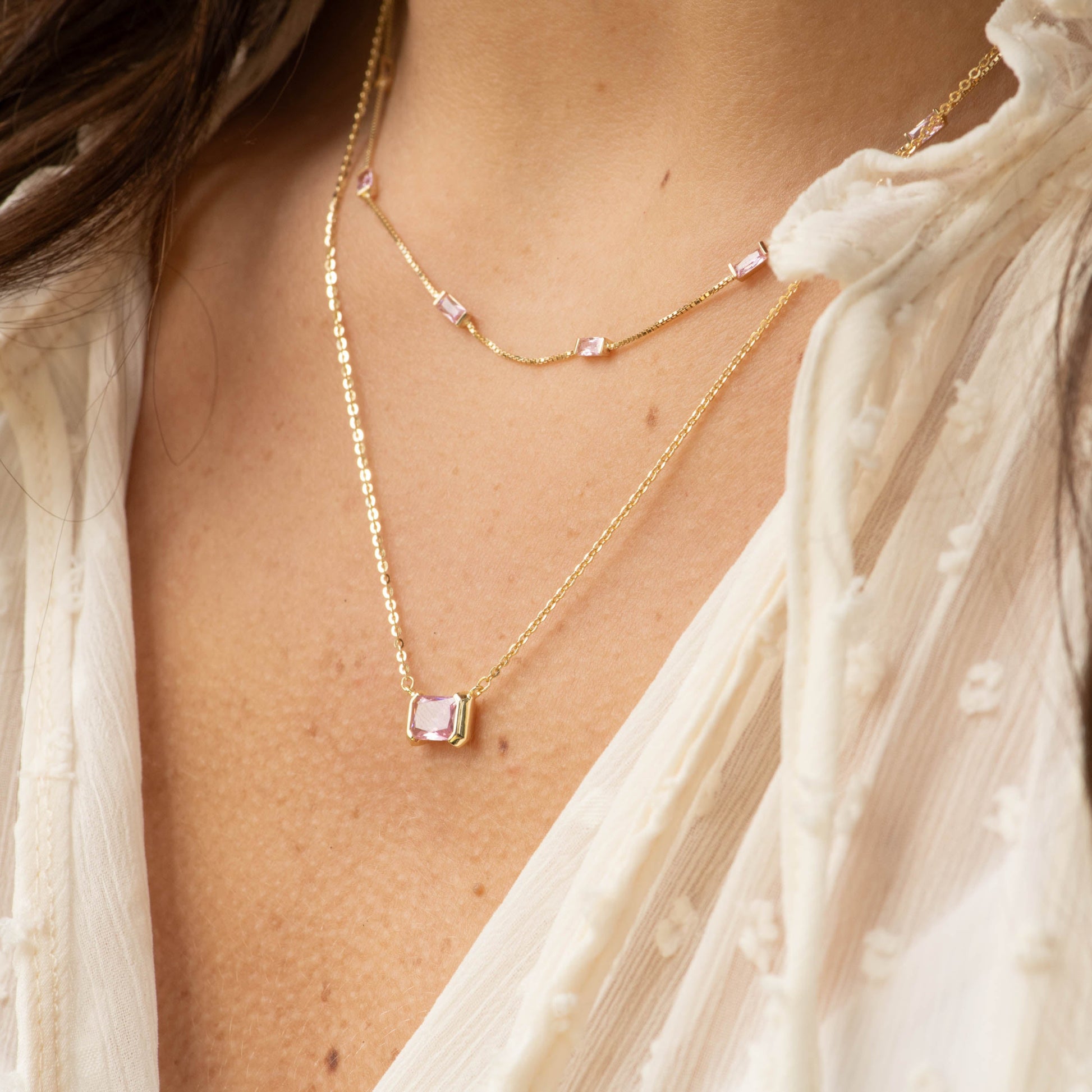 Necklace with a square pendant worn by a person in a light-colored outfit.