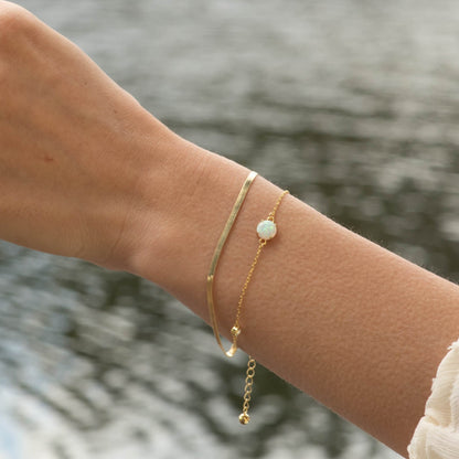 Gold bracelet with small opal-like charm and dangling bead drops