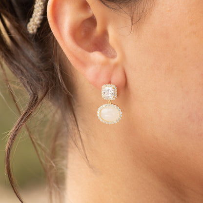 Gold-tone gemstone drop earrings on ear, square clear top and oval white halo bottom