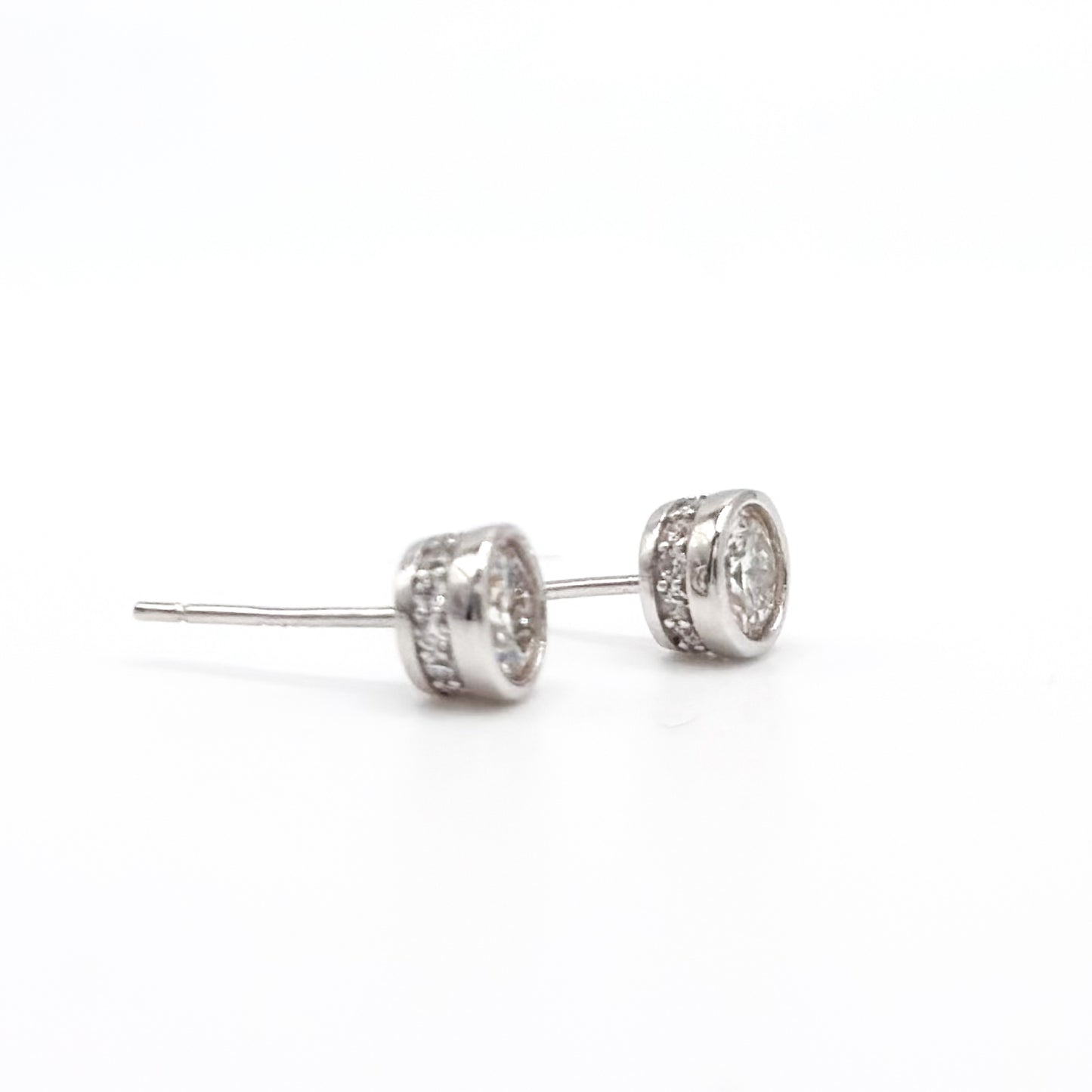 Round moissanite stud earrings with visible posts and bezel-set stones, silver-tone