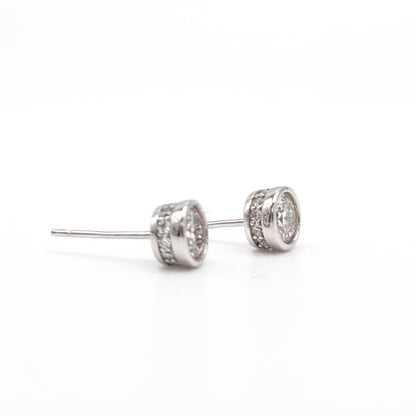 Round moissanite stud earrings with visible posts and bezel-set stones, silver-tone