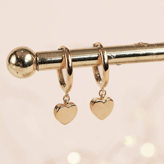 Gold hoop earrings with heart-shaped charms on a light pink background
