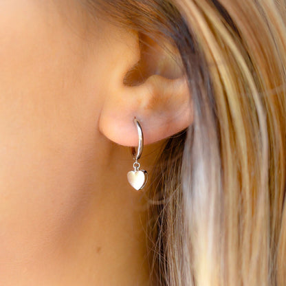 Silver heart huggie earrings on ear, with small heart drop and hoop