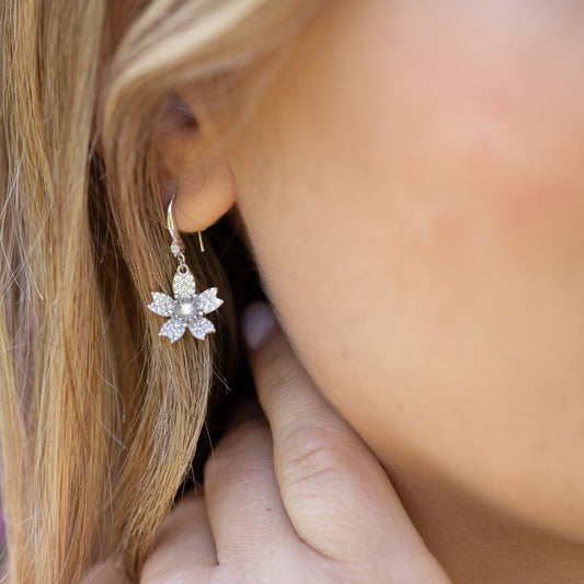 Close-up of a person wearing a silver floral earring with a blurred background