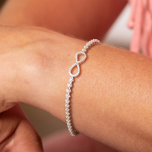 Silver bracelet with infinity design on a wrist against a blurred background