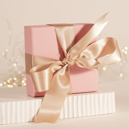 Pink gift box with gold satin bow ribbon on white pedestal