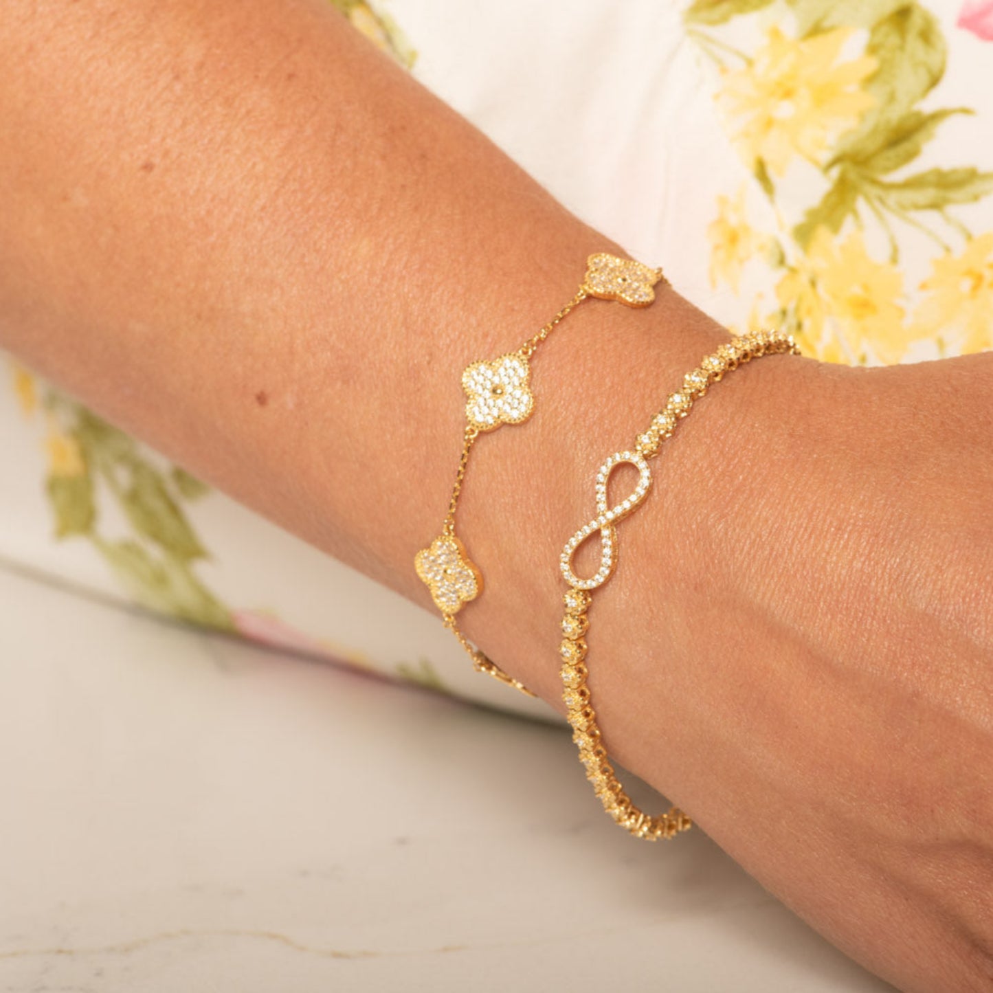 Gold bracelets on a wrist with a floral-patterned background