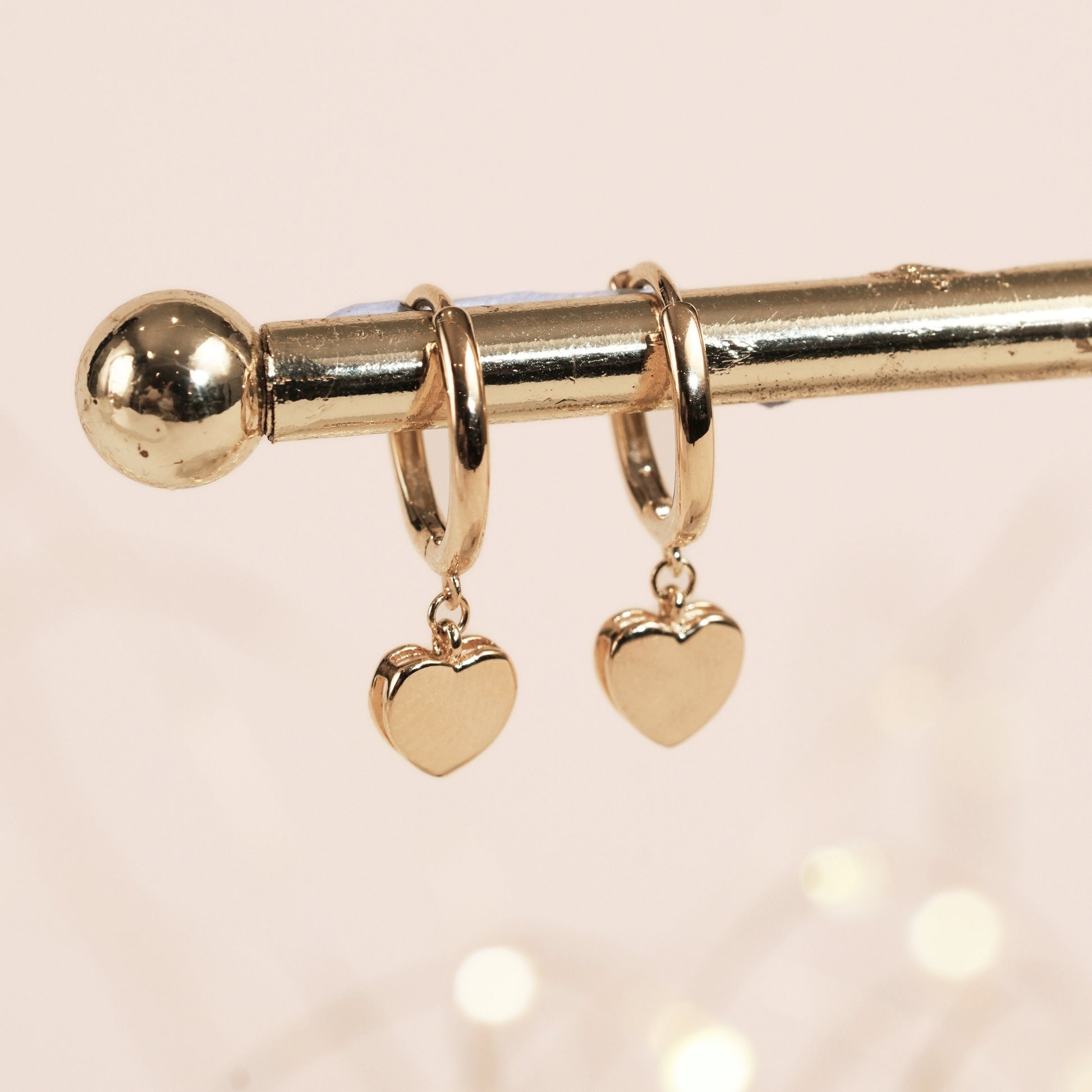 Gold hoop earrings with heart-shaped charms on a light pink background